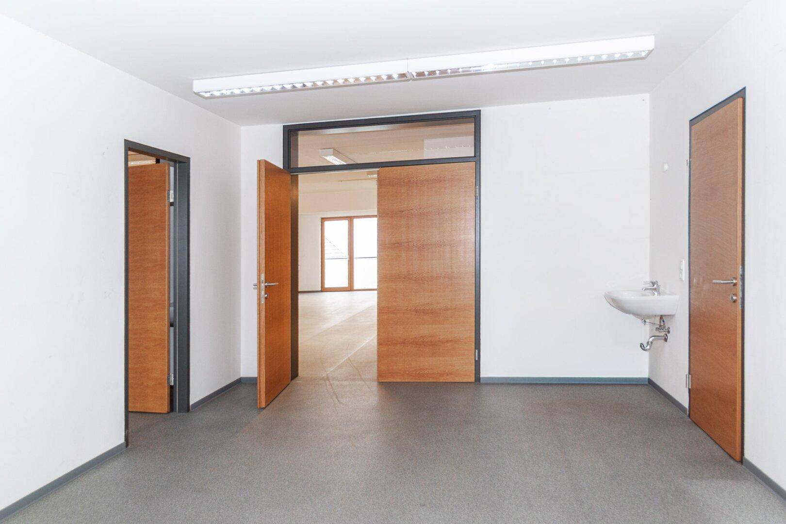 Geräumiger, heller Raum mit Waschbecken und mehreren Holztüren, geeignet für Bürozwecke.