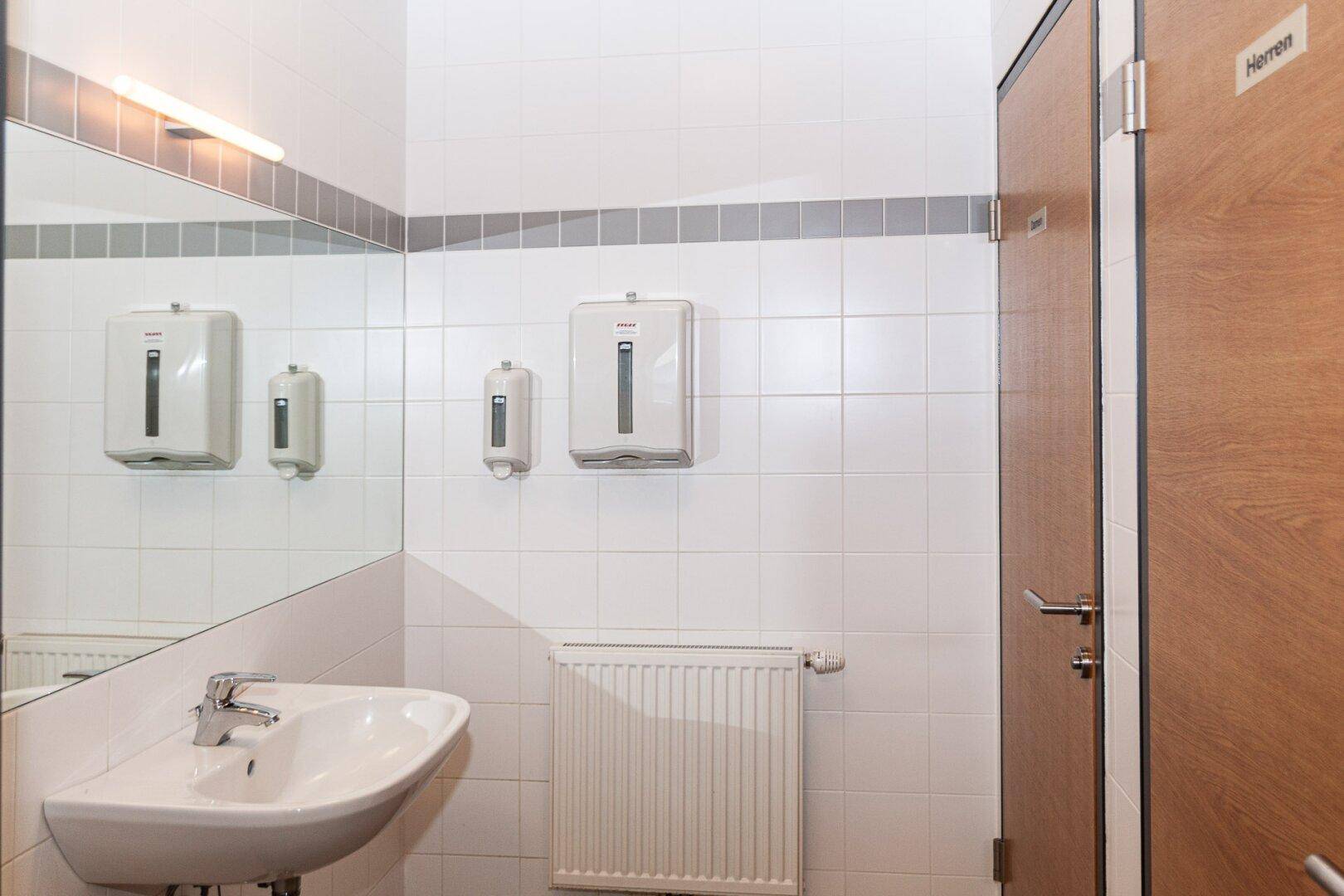 Saubere Toilette mit Waschbecken, Spiegel, Heizkörper und weißen Fliesen.