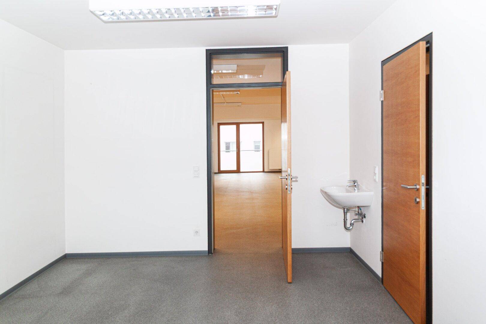 Heller Raum mit Waschbecken und Holztüren, der als Büro oder Teeküche genutzt werden könnte.