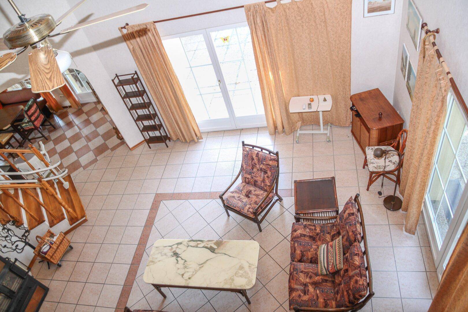 Blick von oben auf das offene Wohnzimmer mit Fliesenboden und hohen Decken.