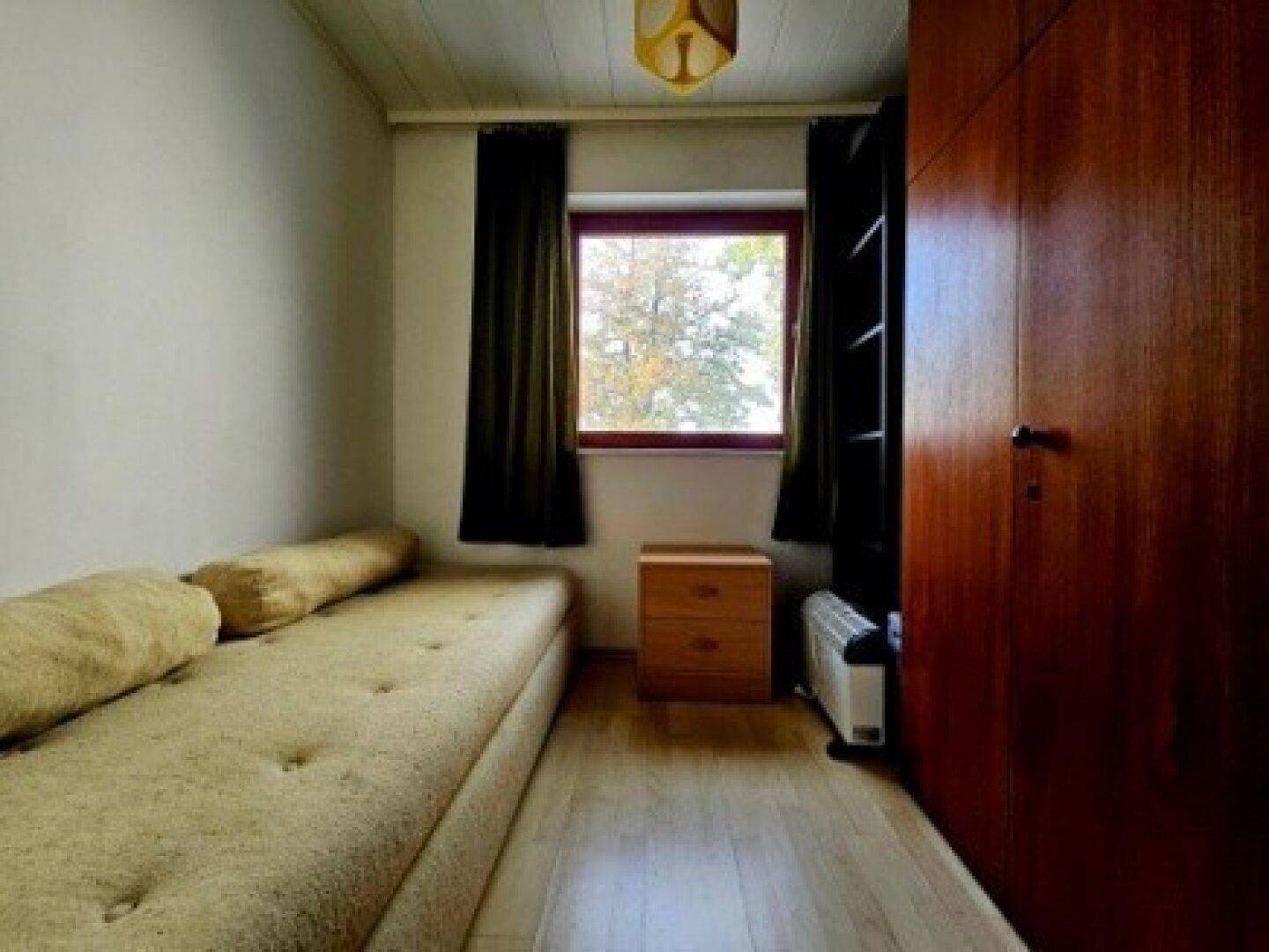 Kleines Schlafzimmer mit Einzelbett, Holzschrank und Fenster mit Blick ins Grüne.