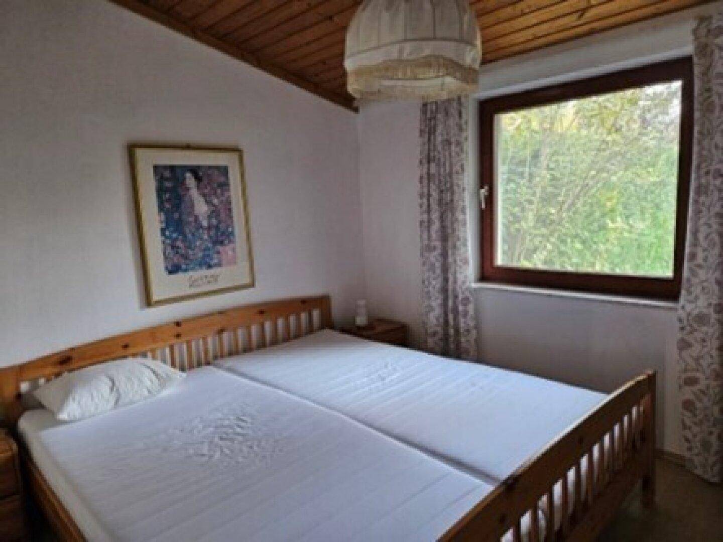 Gemütliches Schlafzimmer mit zwei Einzelbetten, Holzdecke und Blick ins Grüne.