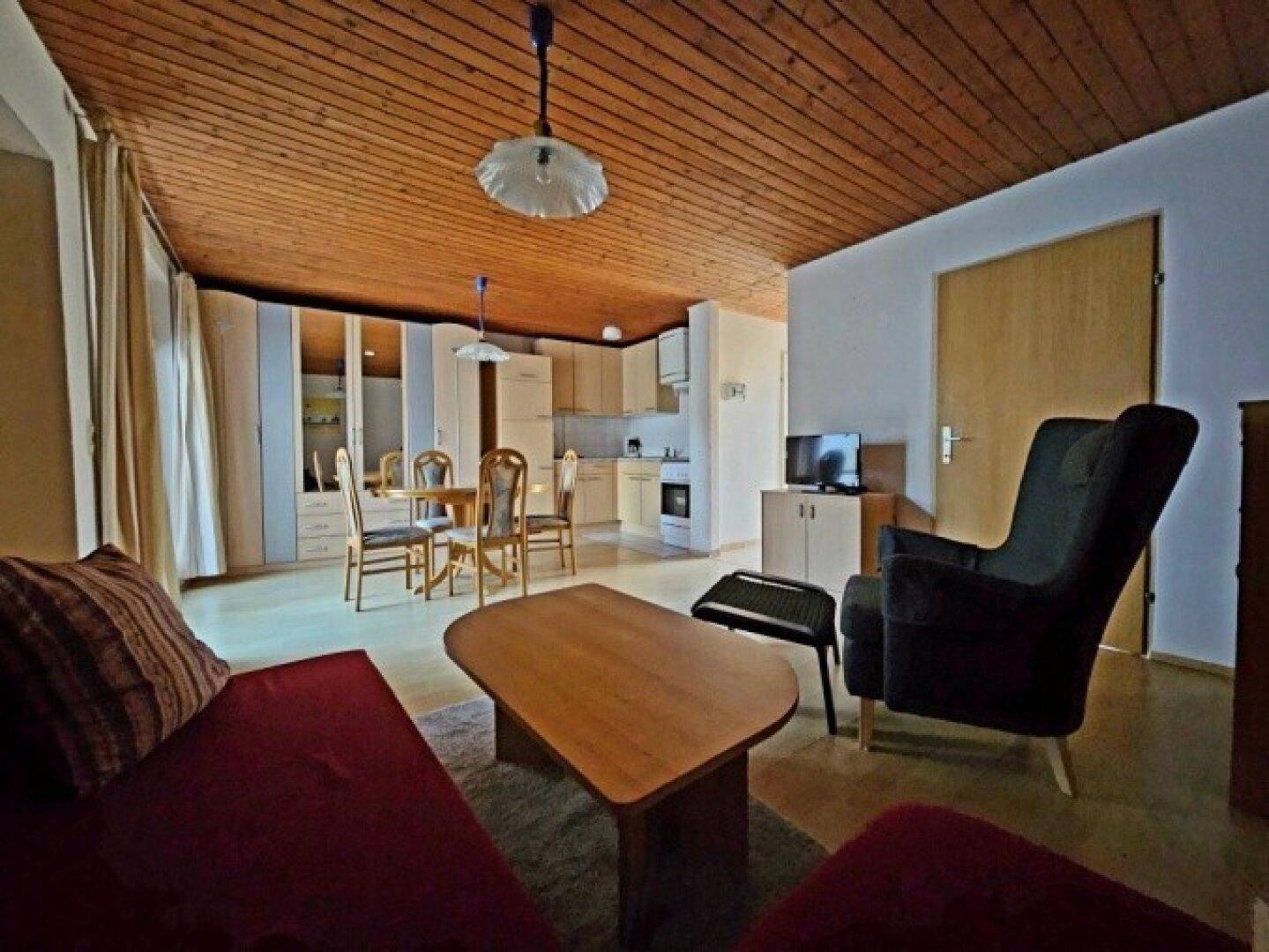 Offener Wohn- und Essbereich mit rotem Sofa, Holzdecke und integrierter Küchenzeile.