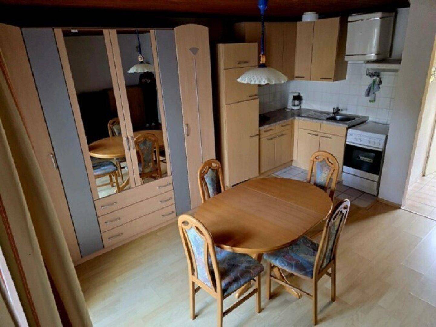 Essbereich mit Holztisch und Stühlen, angrenzend an eine kompakte Küche mit Einbauschränken.
