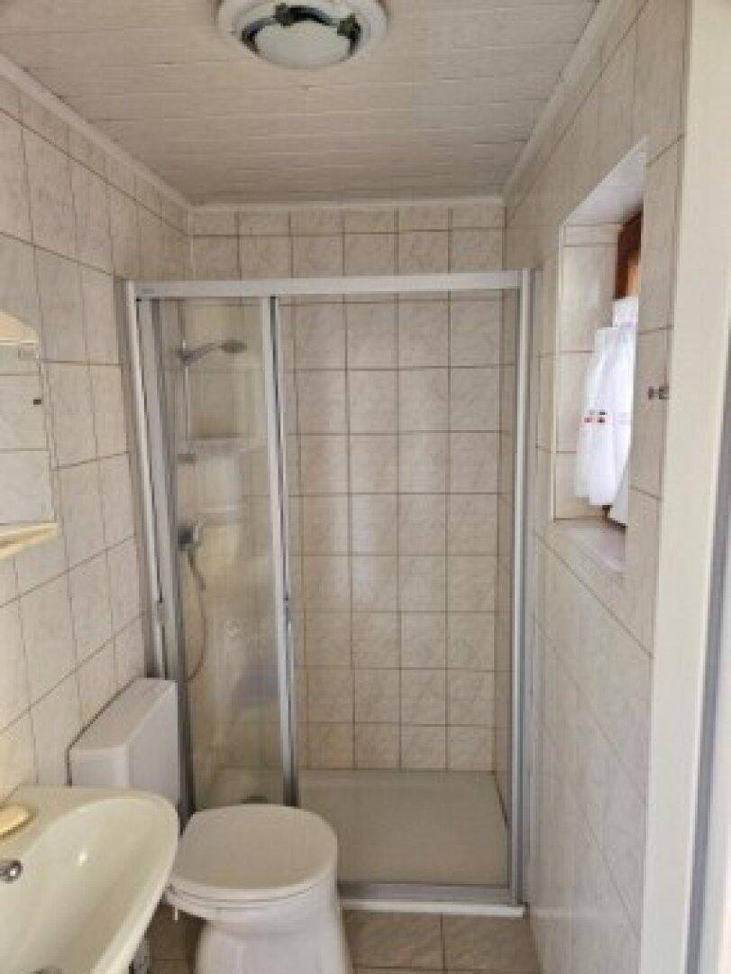 Gefliestes Badezimmer mit Duschkabine, WC, Waschbecken und kleinem Fenster.