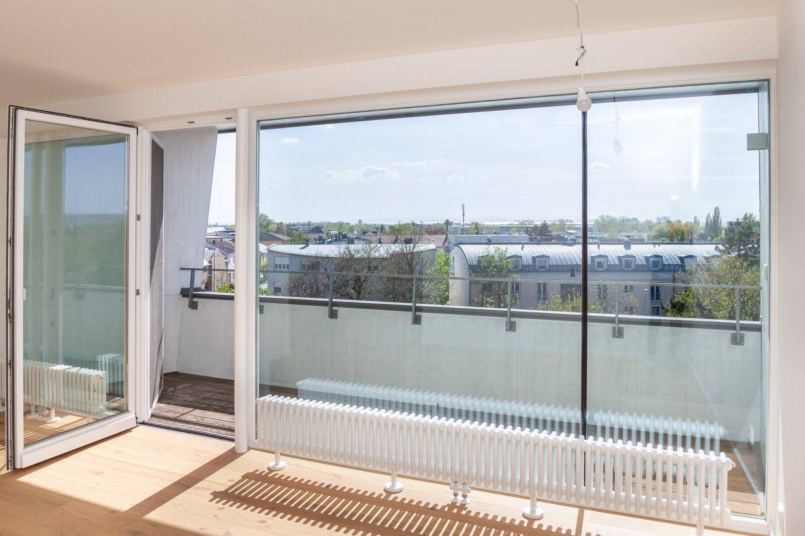 Heller Raum mit großen Fenstern, Holzboden und Zugang zu einem Balkon mit Stadtblick.