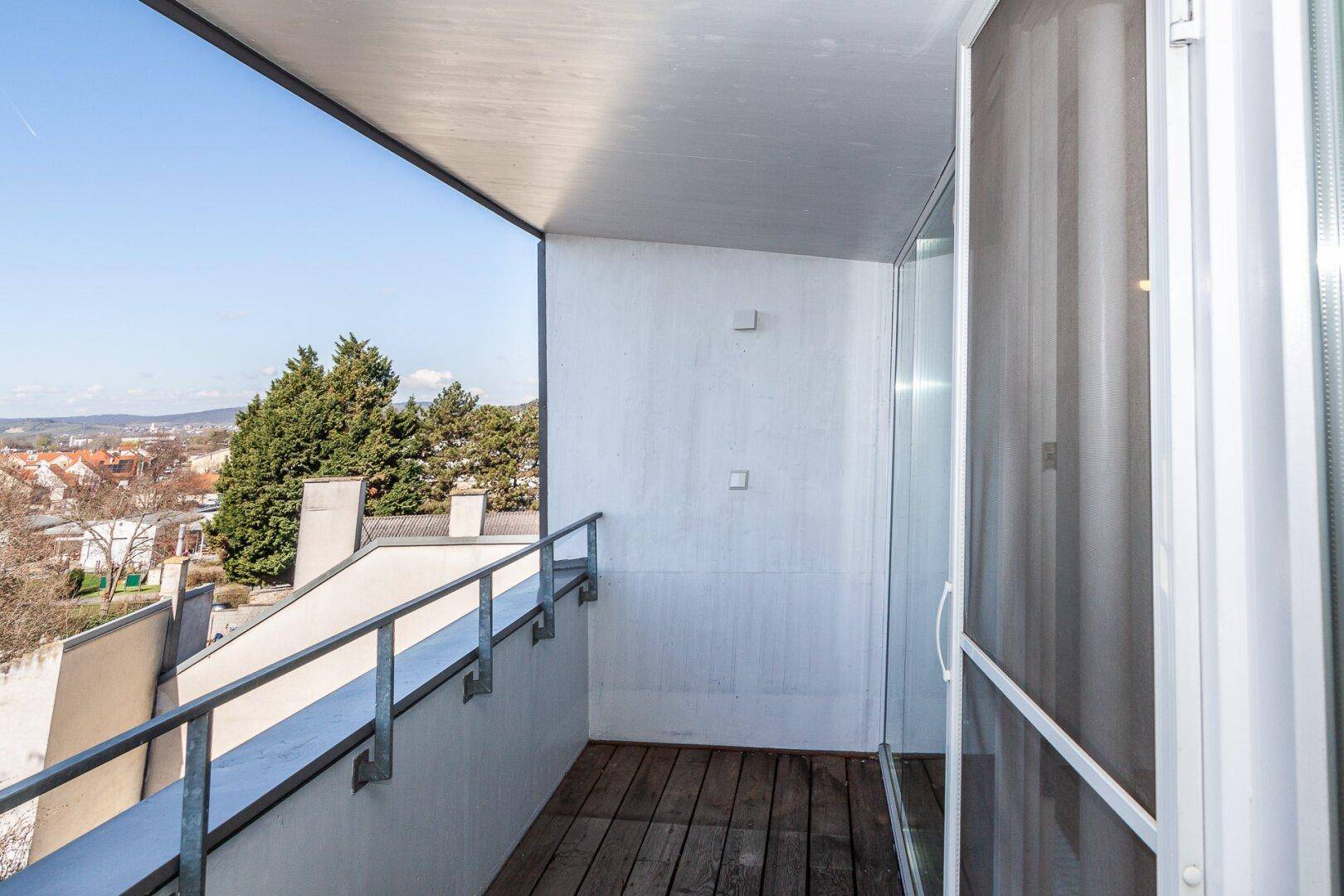 Schmaler Balkon mit Holzboden und weitem Blick über die Dächer und grüne Umgebung.