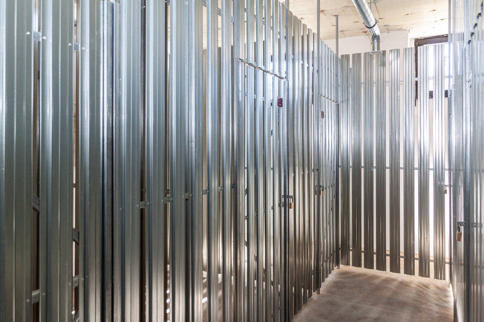 Reihe von Kellerabteilen mit Metallwänden und Betonboden in einem Gemeinschaftsraum.