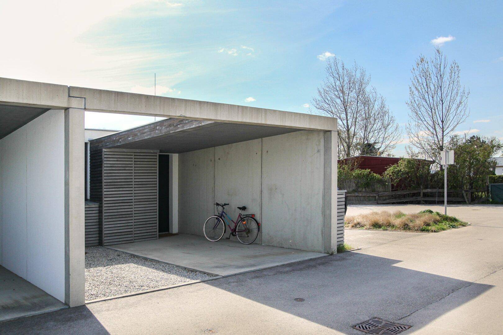 Heller Carport aus Beton mit Stellplatz und Fahrradabstellmöglichkeit.