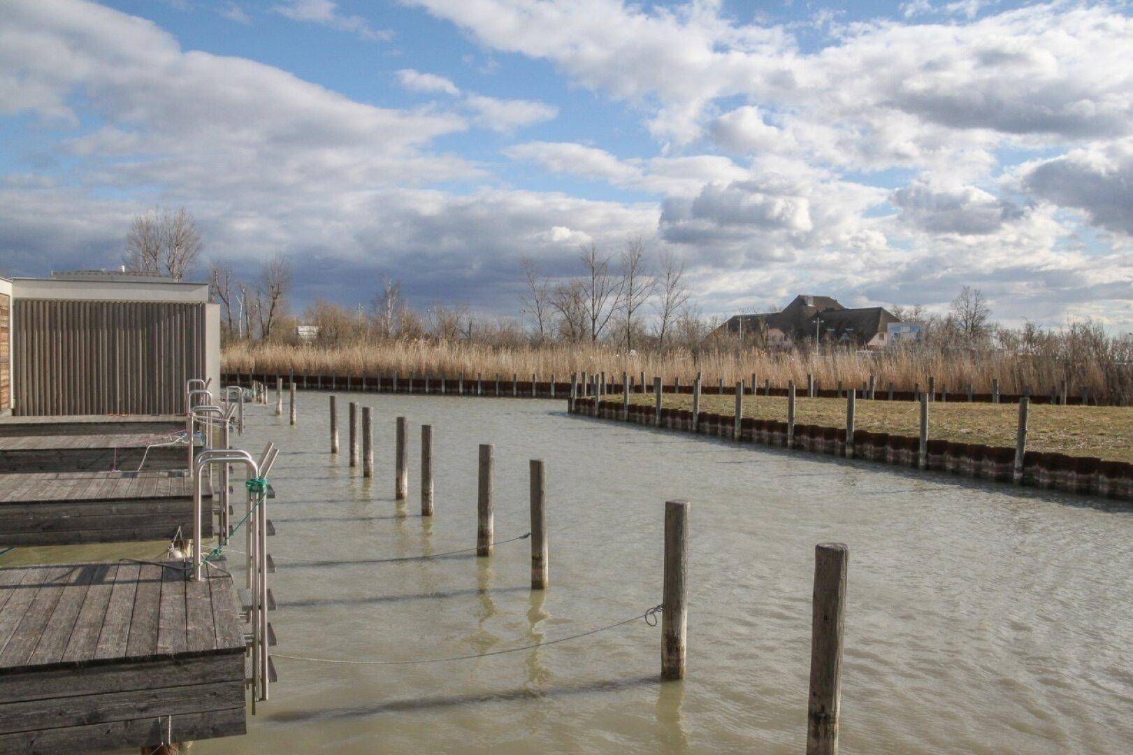 Ruhiger Kanal mit Bootsanlegestellen und natürlicher Ufervegetation.