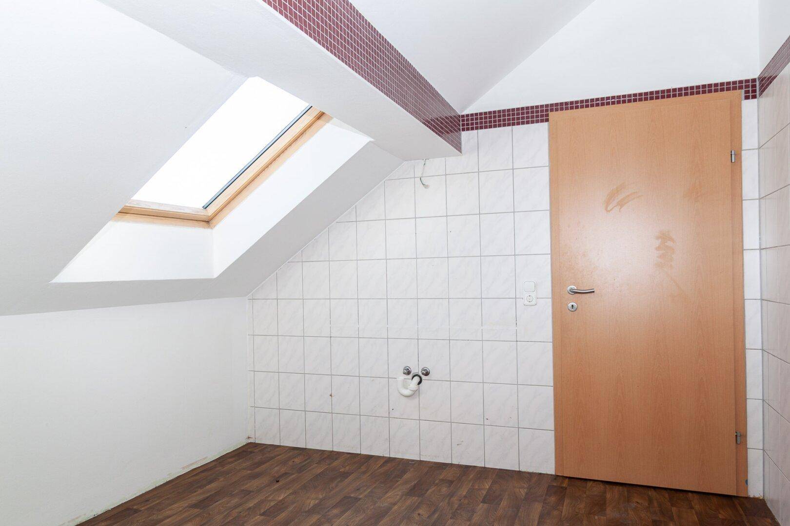 Badezimmer im Dachgeschoss mit Dachfenster, weißen Fliesen und vorbereiteten Anschlüssen.