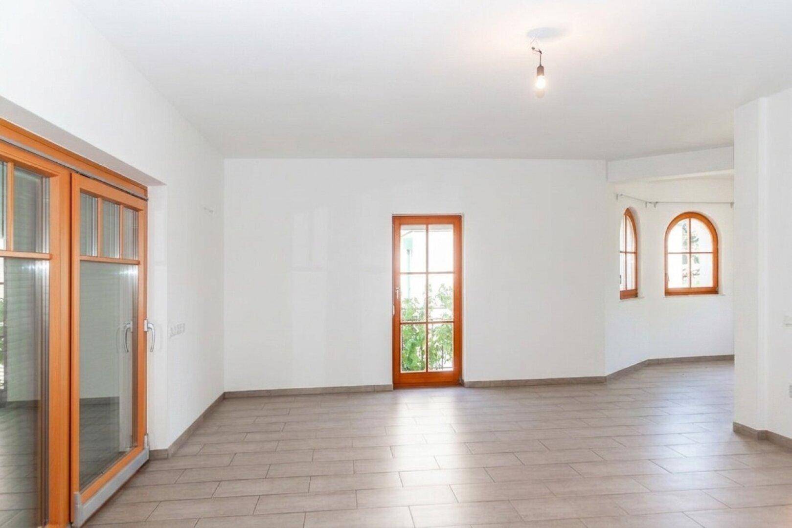 Geräumiges Wohnzimmer mit Fliesenboden, großen Fenstern und Zugang zur Terrasse.