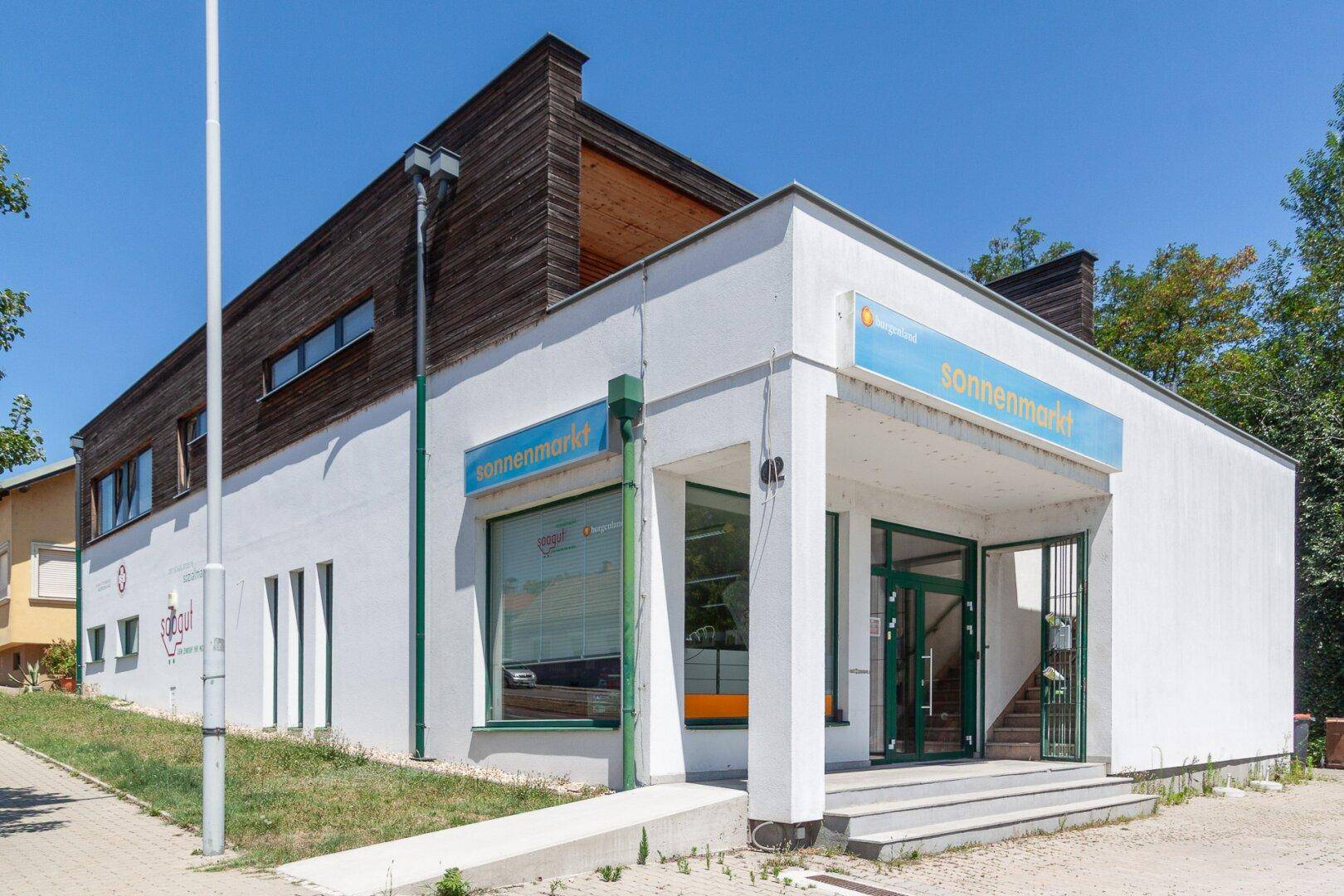 Seitenansicht des Gebäudes mit Eingangsbereich, Rampe und Holzfassade bei Sonnenschein.