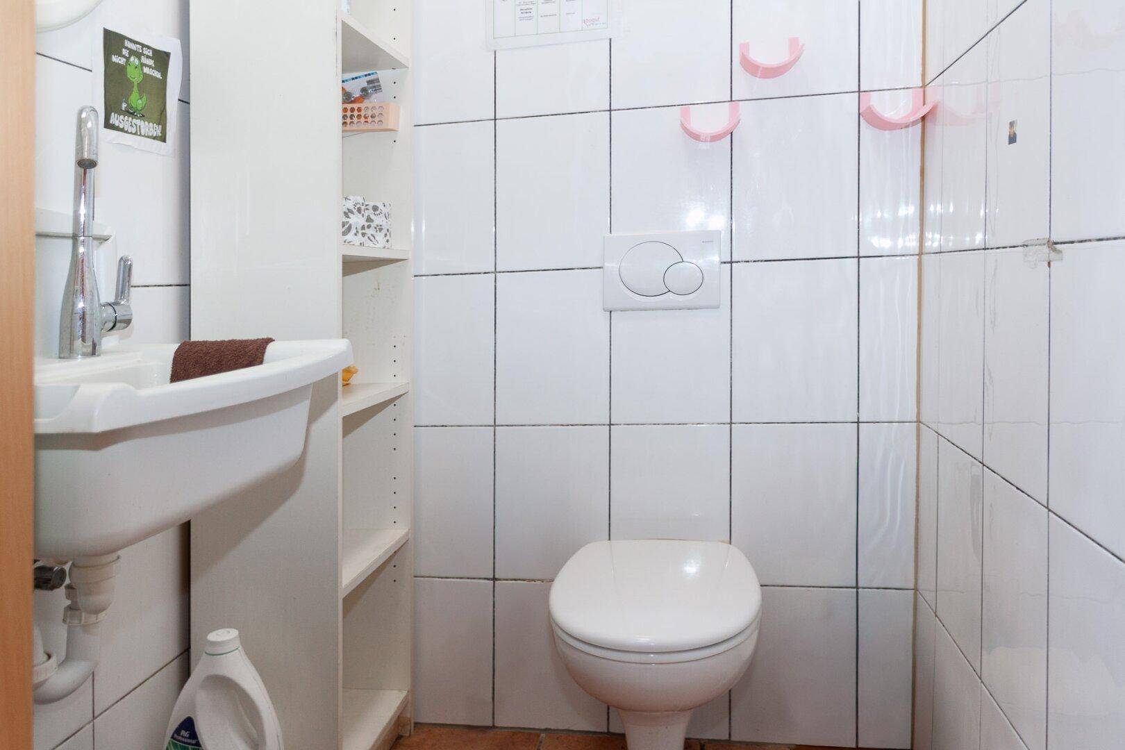 Kleines Gäste-WC mit weißen Fliesen, Toilette und Waschbecken.