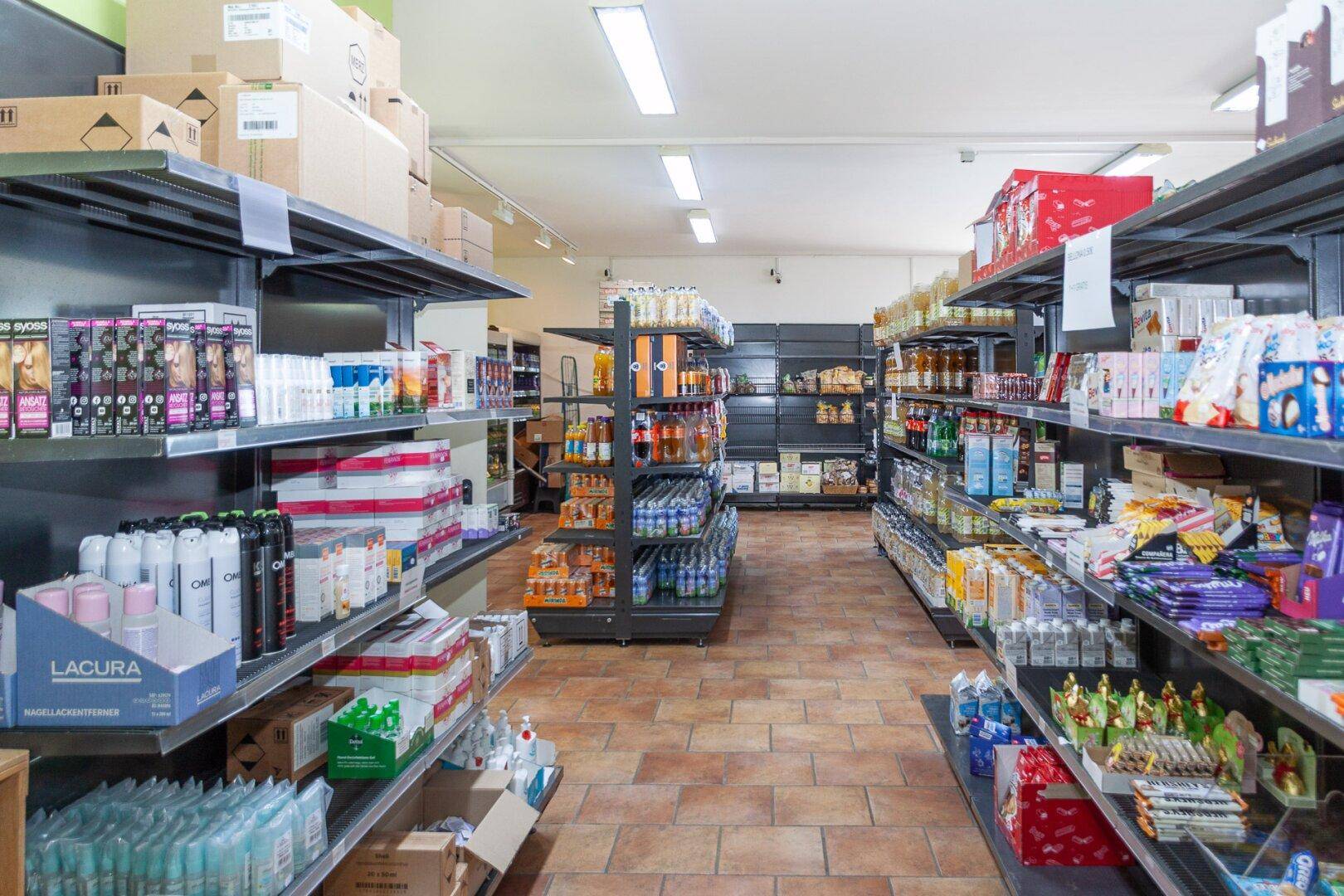 Gang in einem Supermarkt mit voll bestückten Regalen und Terrakotta-Fliesenboden.