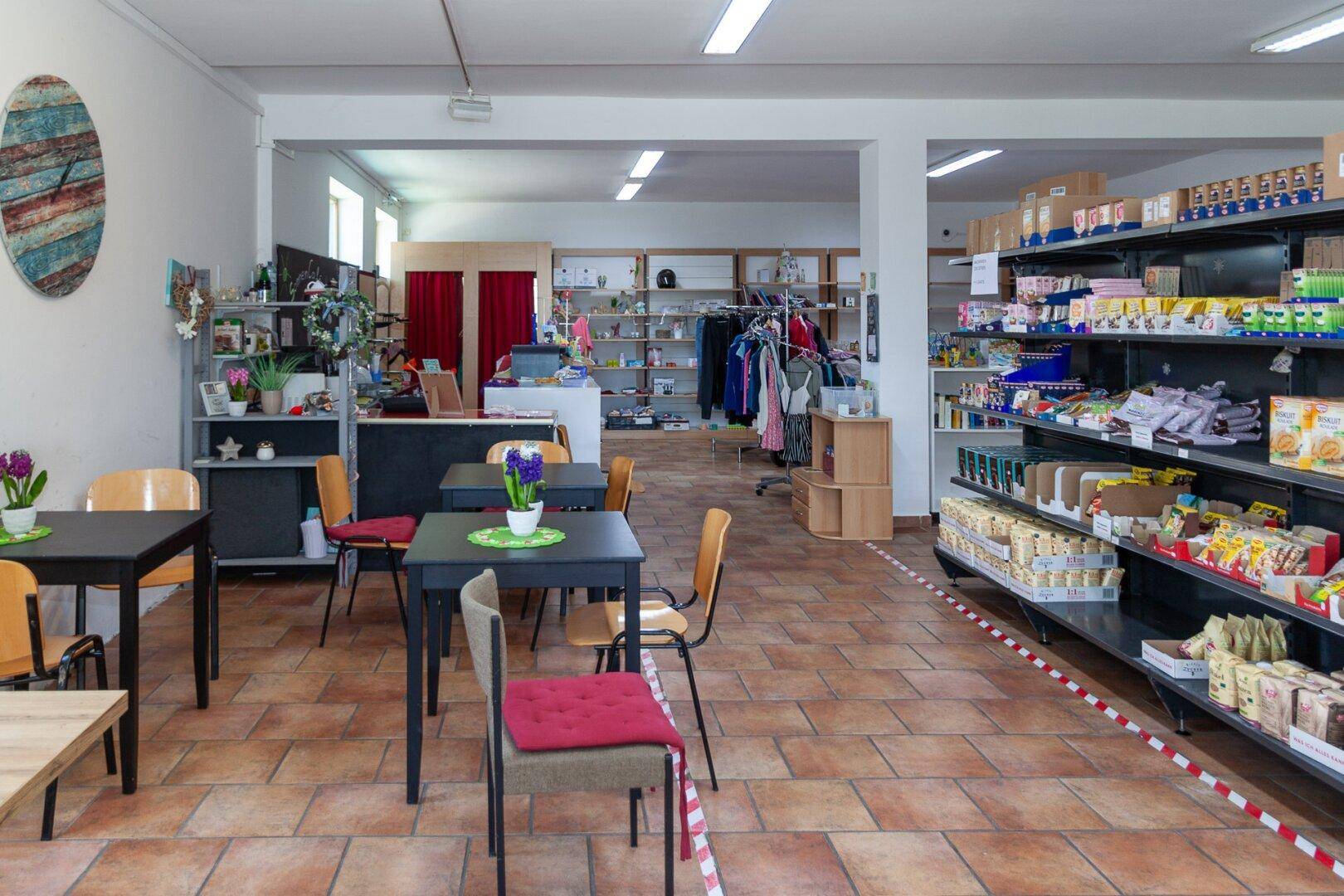 Verkaufsraum mit kleinem Cafébereich, Tischen, Stühlen und Produktregalen.