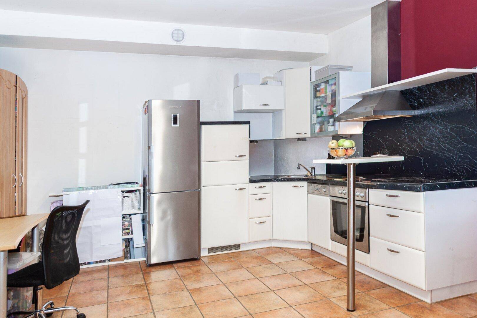 Moderne Küche mit weißen Schränken, schwarzen Arbeitsplatten, großem Kühlschrank und Backofen.