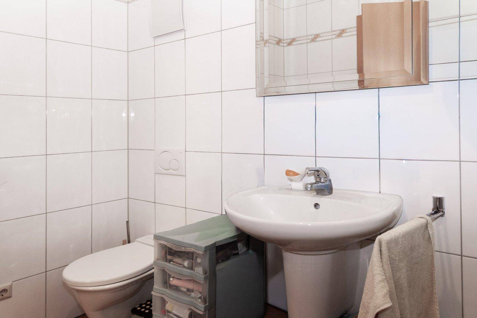 Badezimmer mit weißen Fliesen, Toilette, Waschbecken und Spiegelschrank.