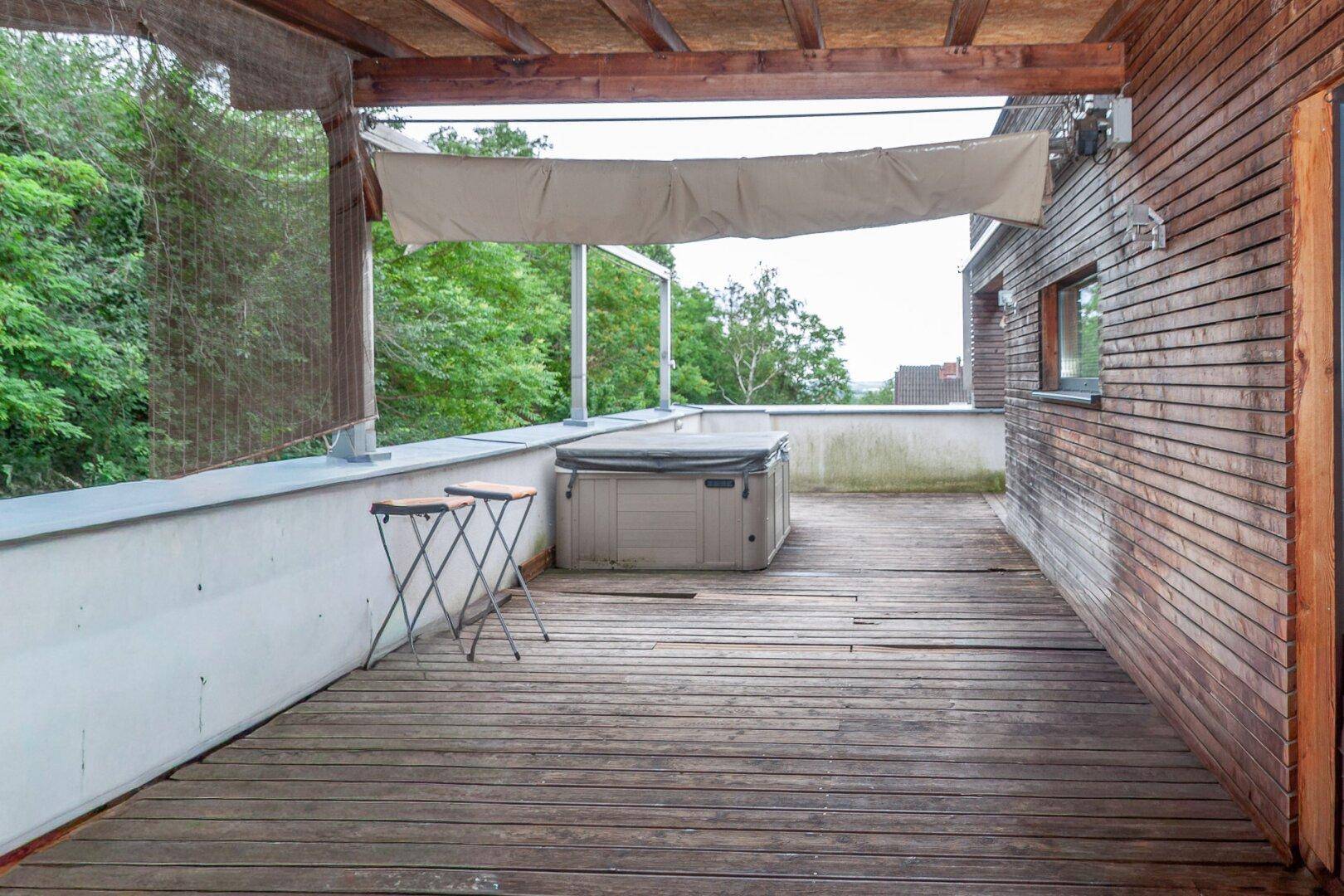 Große Holzterrasse mit Whirlpool und Blick ins Grüne, ideal zum Entspannen.