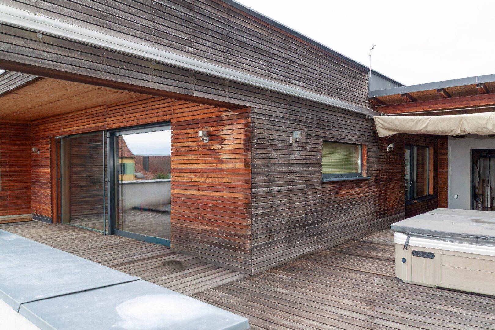 Holzterrasse mit Holzfassade des Gebäudes und einem Whirlpool für entspannte Stunden.