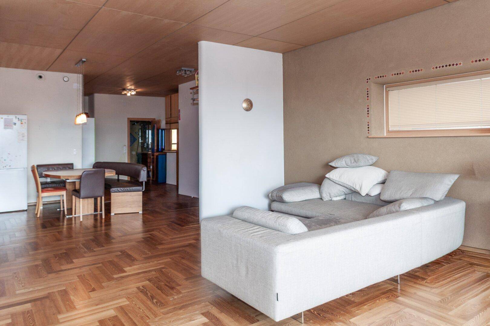 Heller Wohn- und Essbereich mit Fischgrätparkett, beiger Wandfarbe und gemütlichem Sofa.