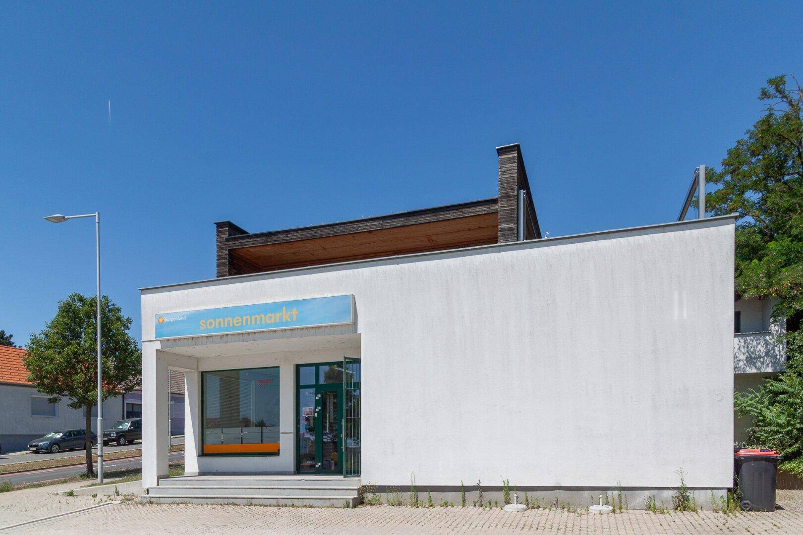 Seitenansicht des Geschäftsgebäudes mit weißer Fassade und Holzverkleidung unter blauem Himmel.