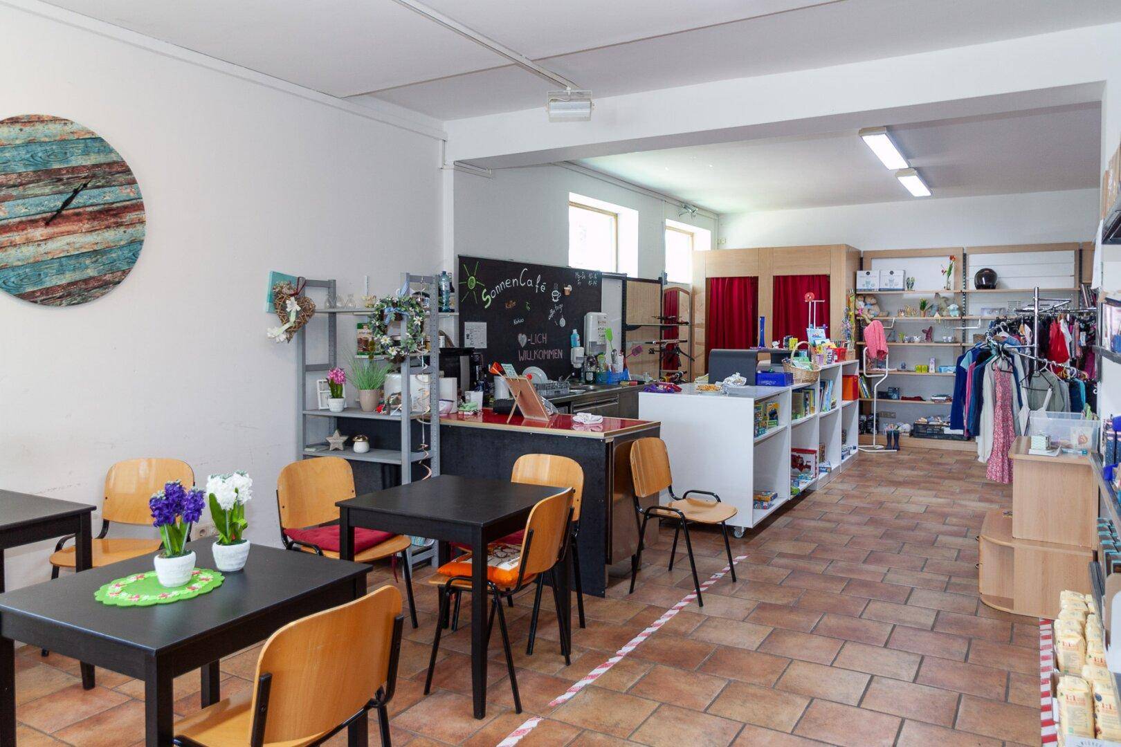 Verkaufsraum mit Café-Bereich, Tischen, Stühlen und Regalen mit verschiedenen Produkten.