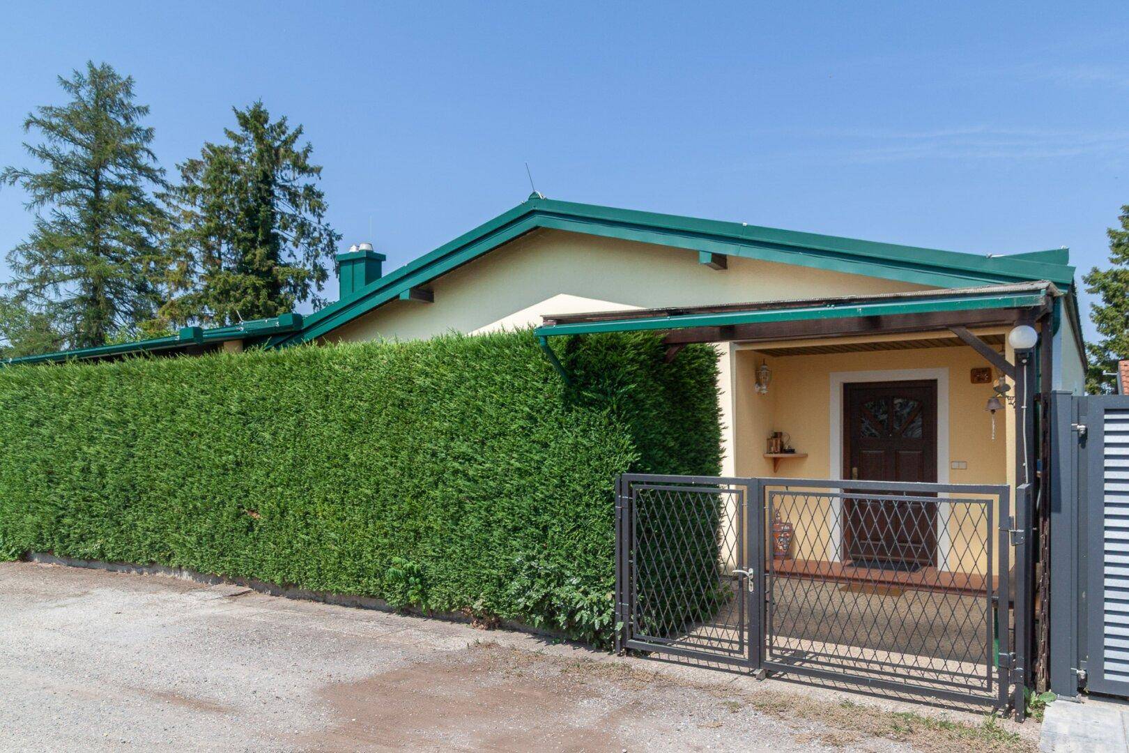 Eingangsbereich eines Hauses mit überdachtem Vorbau, grüner Hecke und modernem Metalltor.