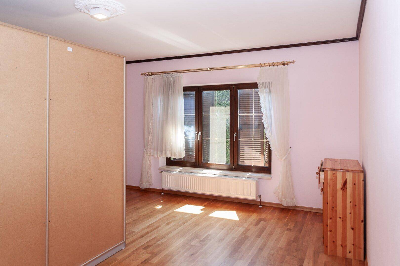 Helles Schlafzimmer mit rosa Wänden, Holzfußboden, großem Fenster und Heizkörper.