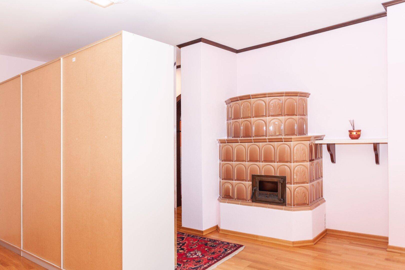 Innenraum mit traditionellem Kachelofen, hellem Holzfußboden und großem Einbauschrank.