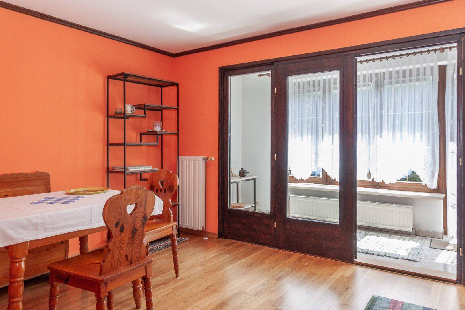 Essbereich mit orangefarbenen Wänden, Holzfußboden und traditionellen Holzmöbeln am Fenster.