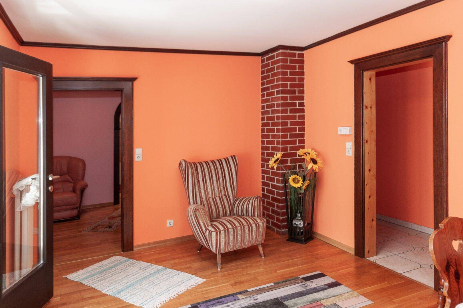 Gemütliches Wohnzimmer mit orangefarbenen Wänden, Holzfußboden und einem bequemen Sessel.