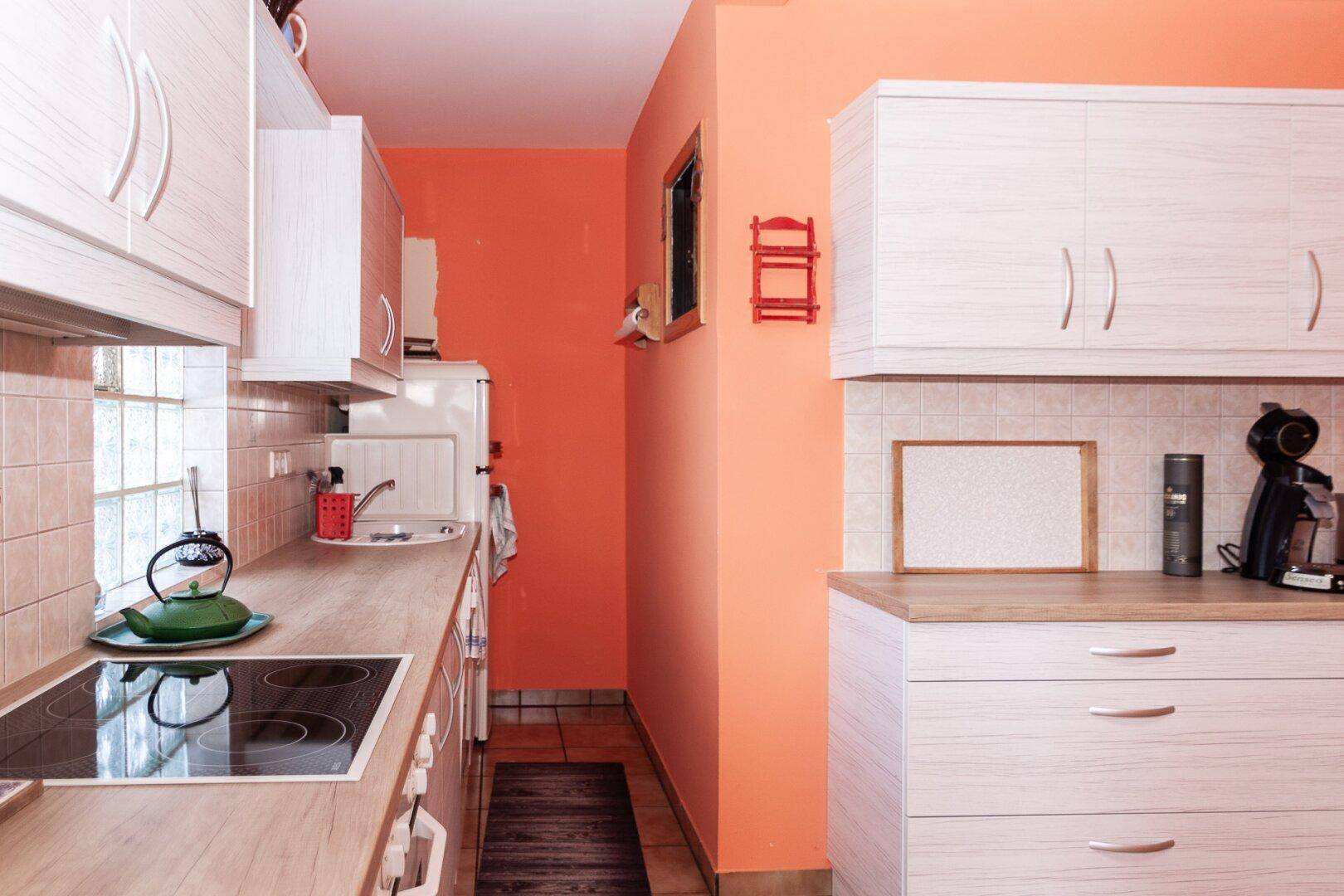 Küche mit orangefarbenen Wänden, hellen Holz-Arbeitsplatten und weißen Hängeschränken.