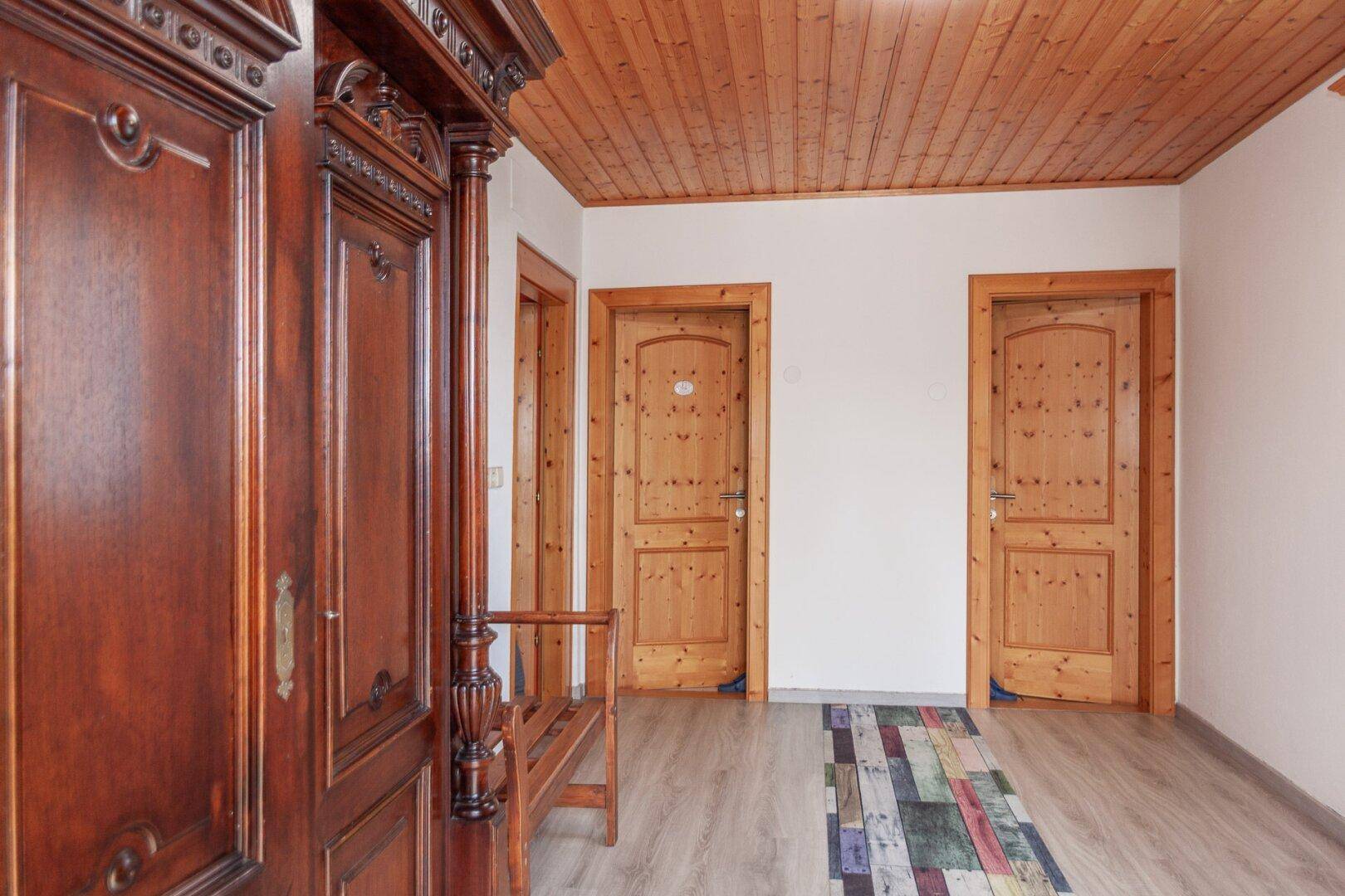 Flur mit Holzdecke, hellem Boden und mehreren Holztüren, sowie einem großen Holzschrank.