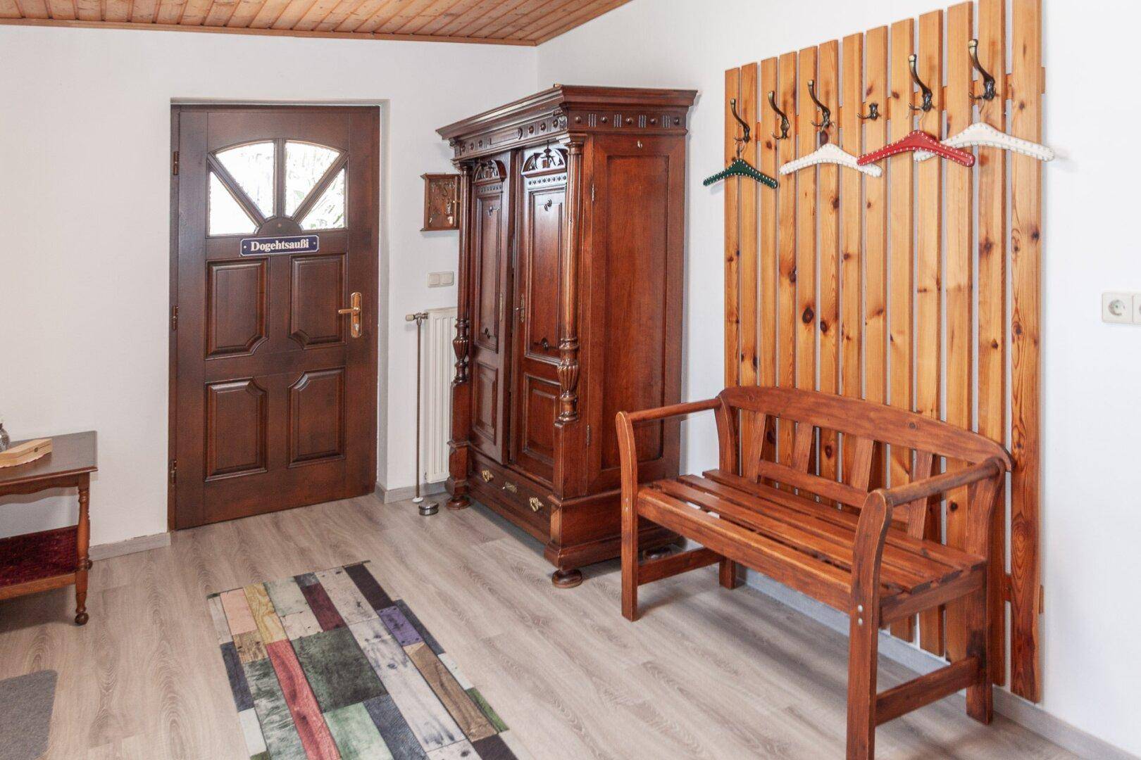 Eingangsbereich mit Holzdecke, heller Boden, Holzbank und Garderobe neben der Eingangstür.