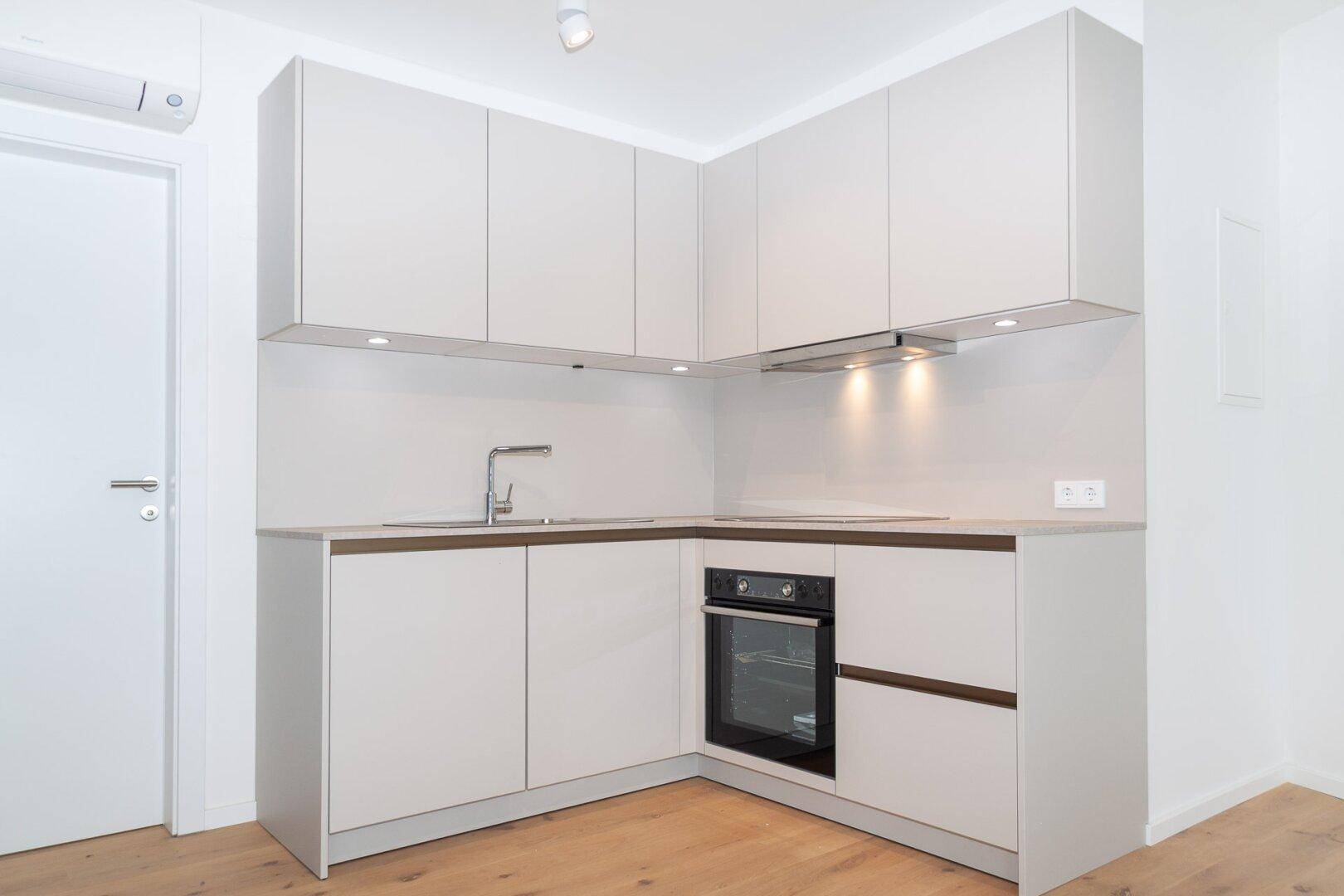 Moderne Küchenzeile mit hellgrauen Schränken, integriertem Backofen und Spülbecken in minimalistischem Design.
