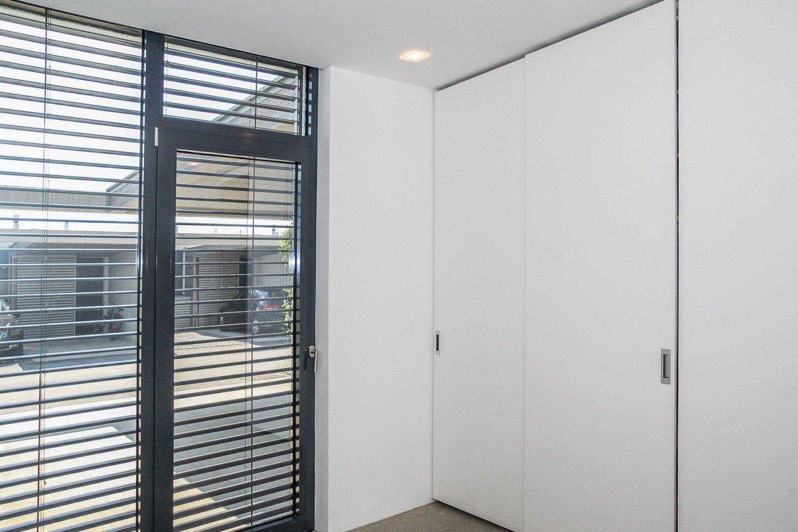 Heller Flur mit integrierten Schränken und einem Fenster mit Jalousien für Privatsphäre.