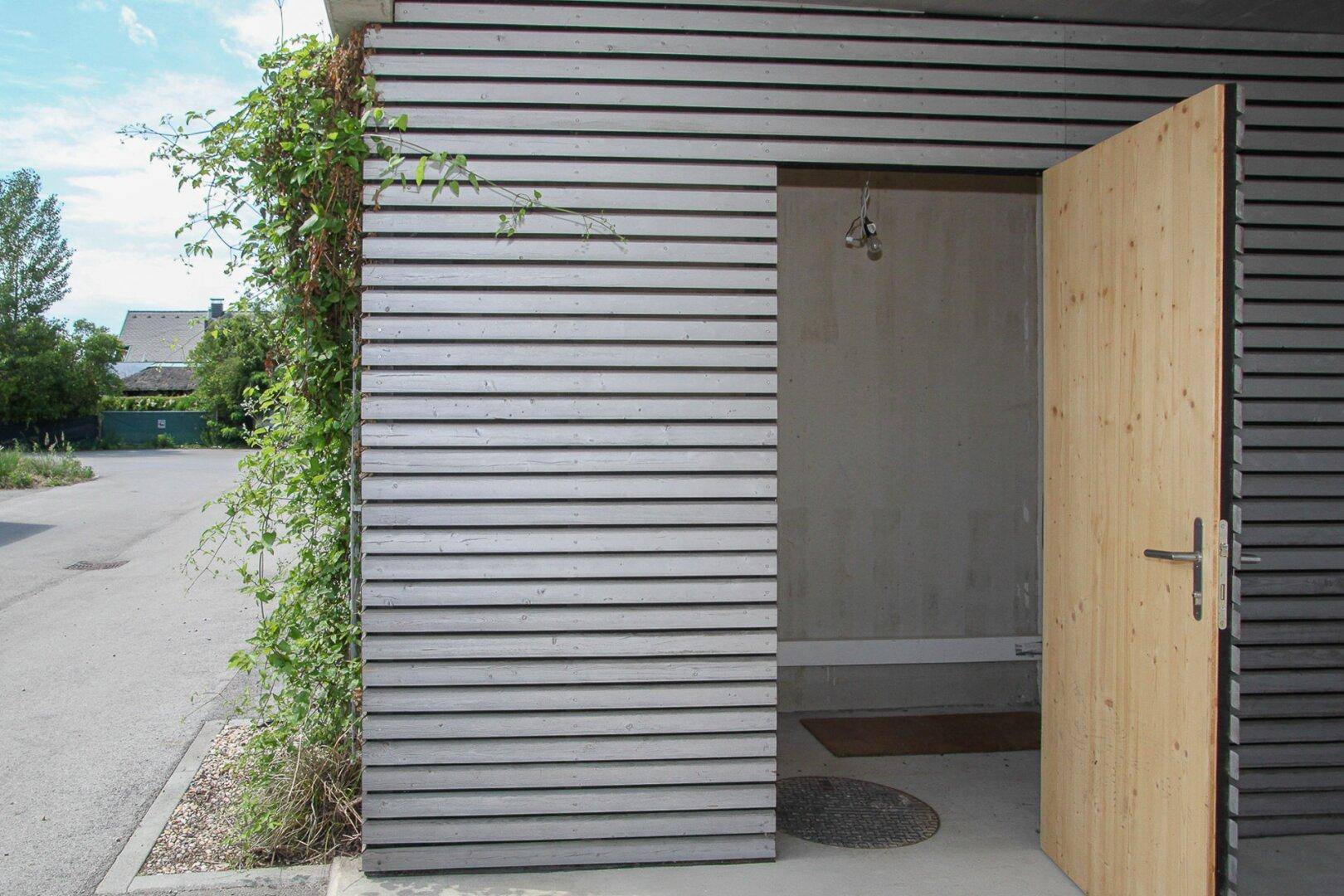 Eingangstür aus hellem Holz in einer modern gestalteten Fassade mit Holzverkleidung.