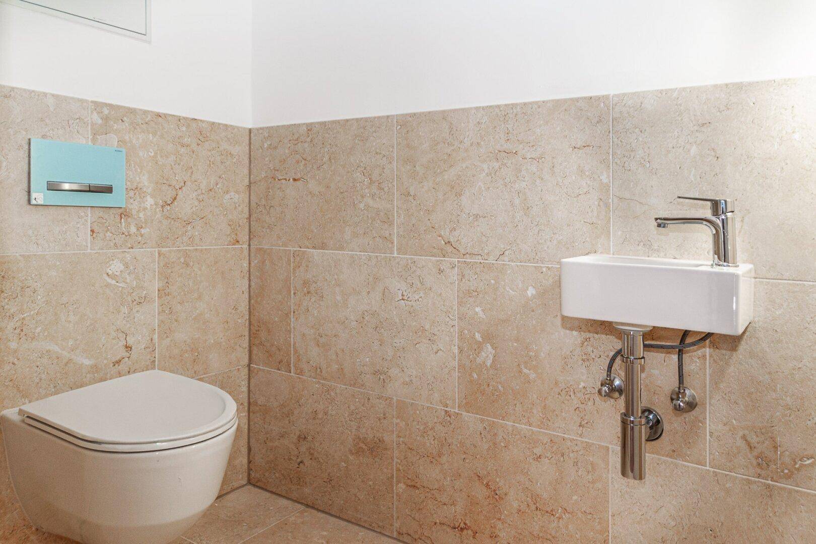 Modernes Gäste-WC mit beigefarbenen Fliesen, wandhängendem WC und kleinem Waschbecken.