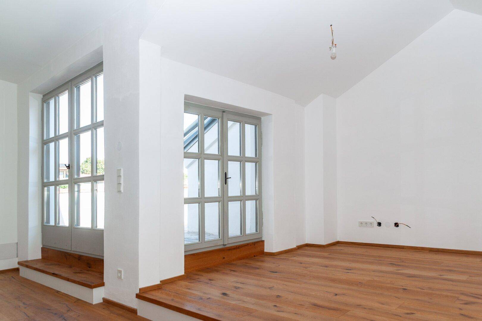 Geräumiger Wohnbereich mit Holzboden, Dachschrägen und großen Fenstern für viel Tageslicht.