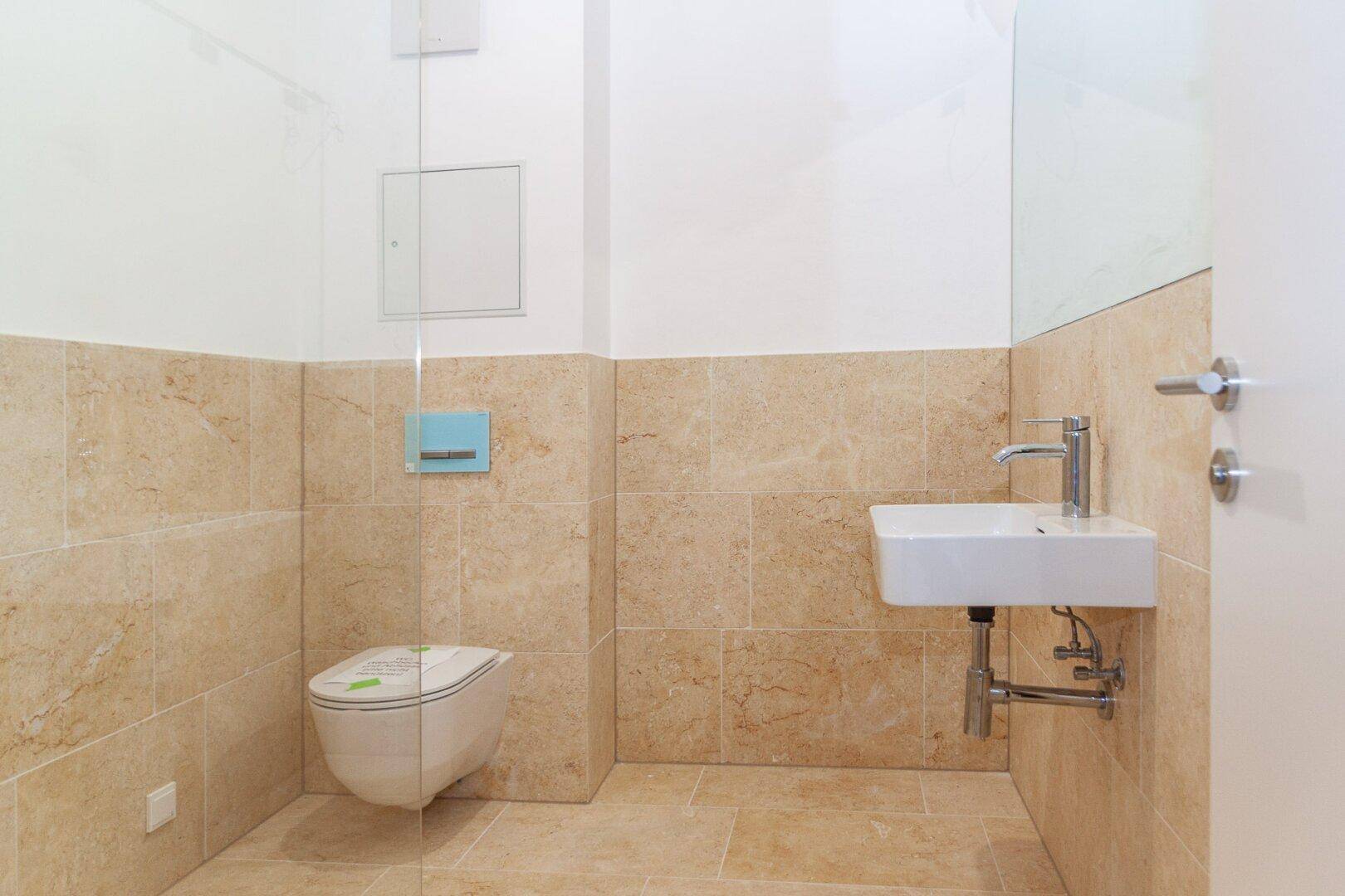 Helles Gäste-WC mit beigefarbenen Fliesen, wandhängendem WC und modernem Waschbecken.