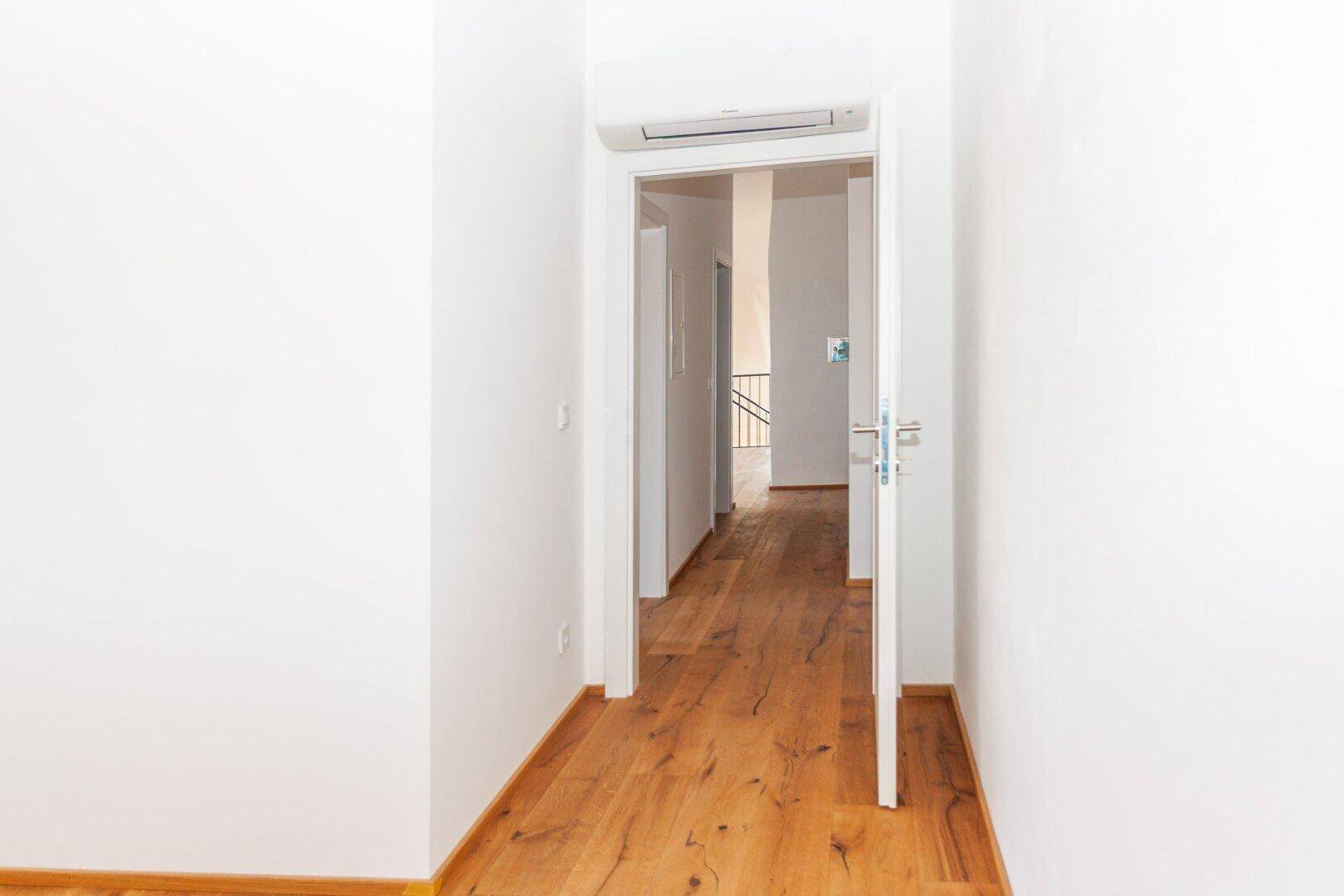 Heller Flur mit Holzboden und offener Tür, die den Blick in weitere Räume freigibt.