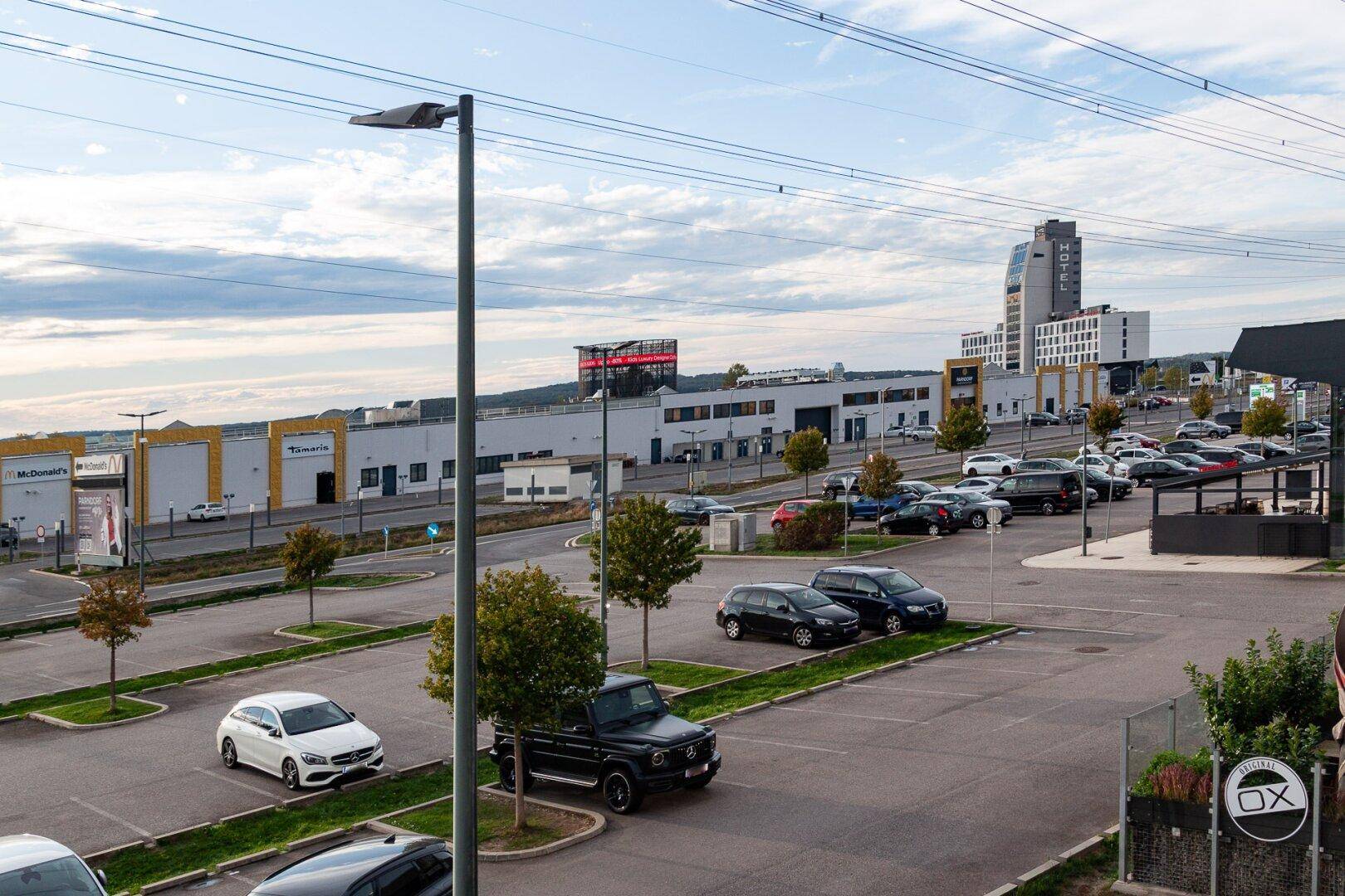 Weitläufiger Parkplatzbereich mit umliegenden Geschäftsgebäuden und einer städtischen Skyline im Hintergrund.