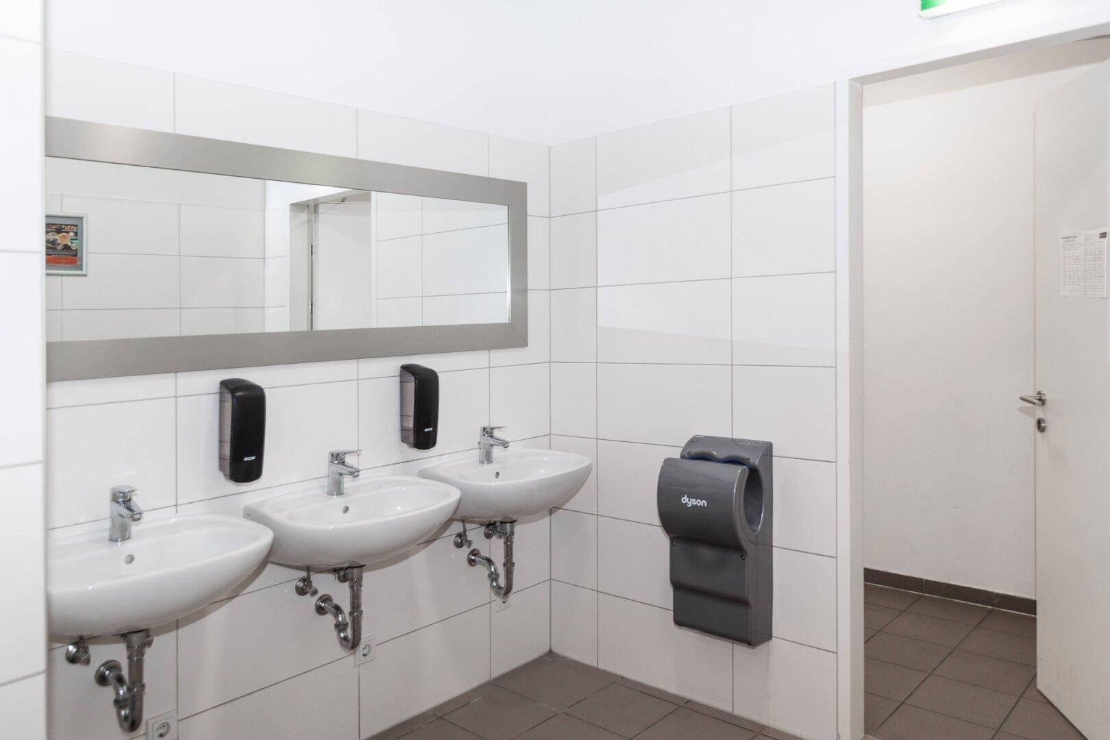 Moderner Waschraum mit drei Waschbecken, großem Spiegel und Dyson Händetrockner.