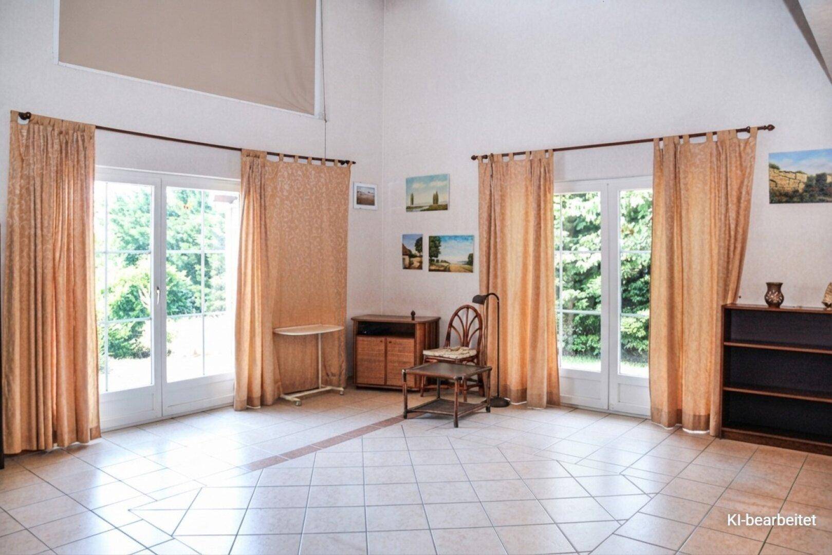 Geräumiges Wohnzimmer mit hohen Decken, großen Fenstern und hellem Fliesenboden.