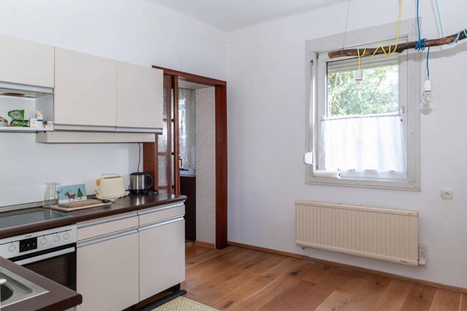 Helle Küche mit beigen Einbauschränken, Holzboden und Fenster, das Tageslicht hereinlässt.