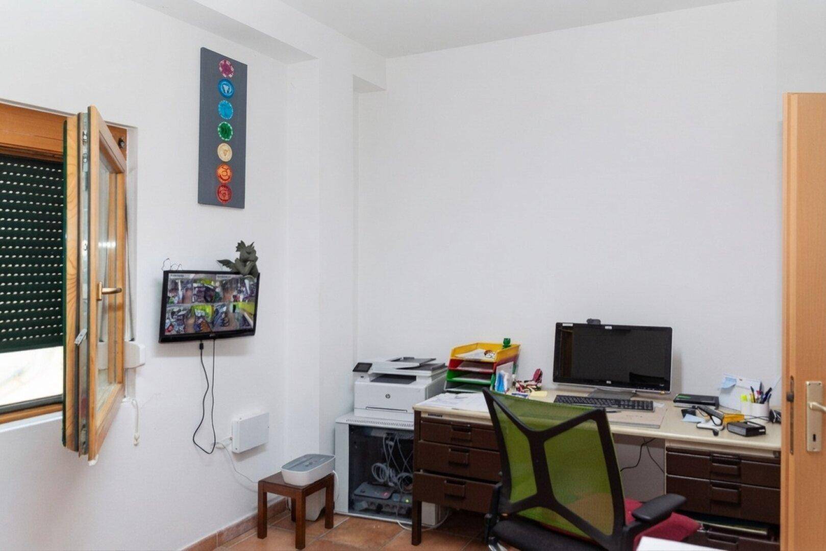 Helles Büro mit Schreibtisch, Computer und einem geöffneten Fenster für natürliche Belüftung.