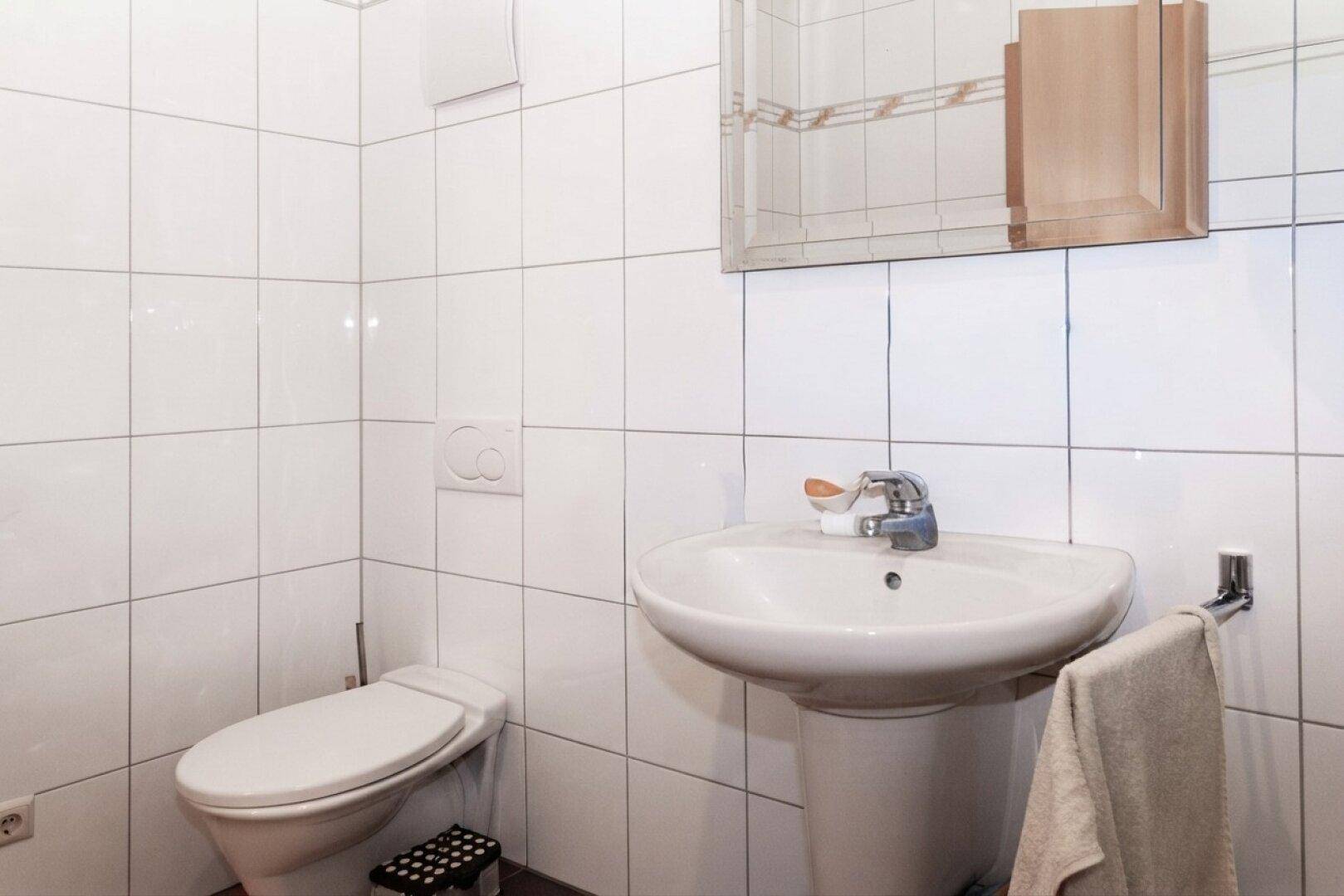 Badezimmer mit weißen Fliesen, einem Waschbecken auf Säule und einer Toilette.