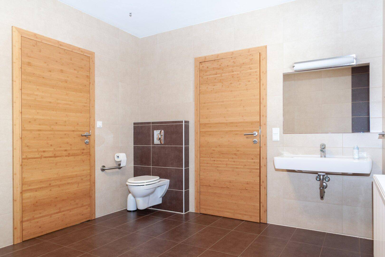 Geräumiges Badezimmer mit zwei Holztüren, wandhängendem WC und modernem Waschbecken.