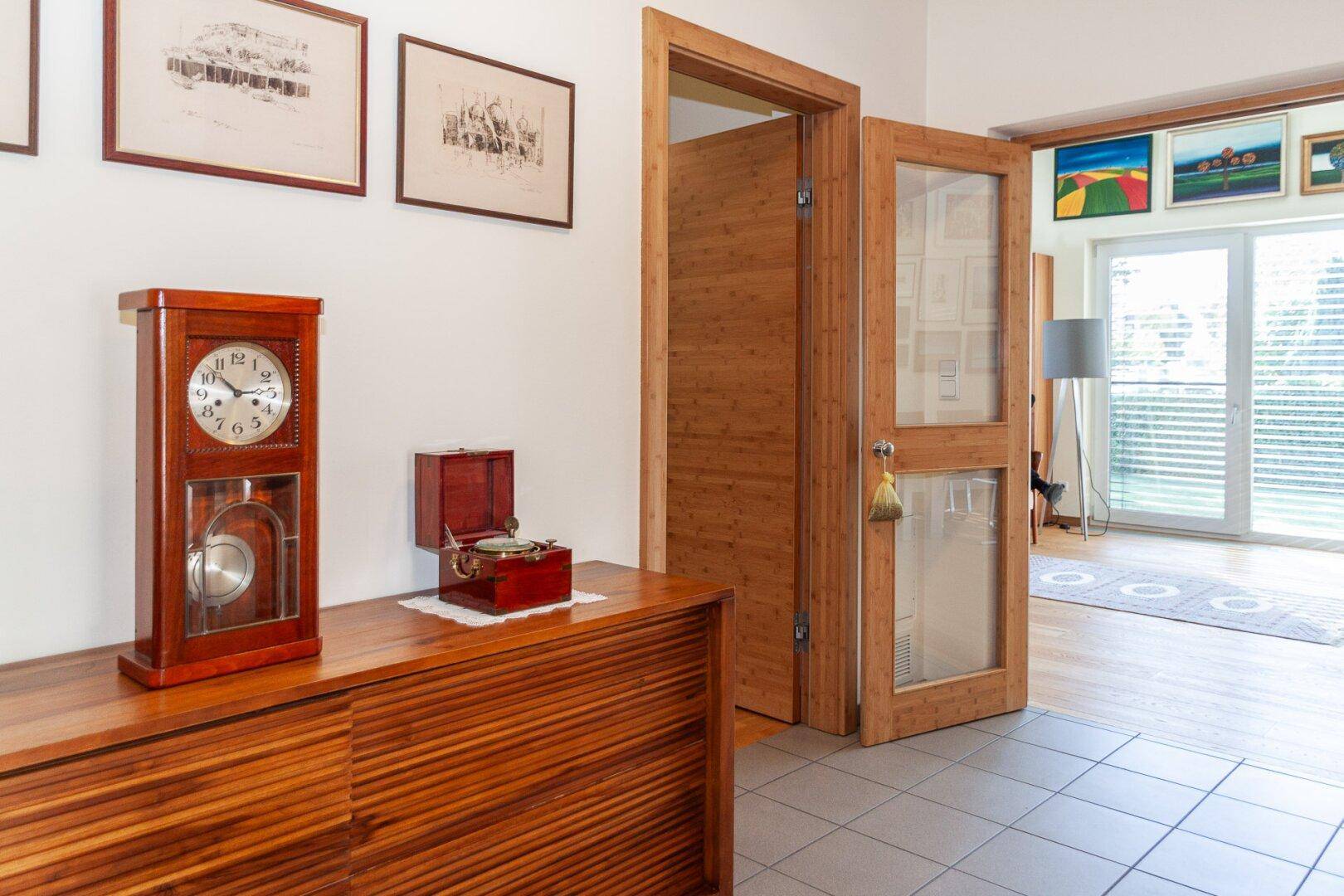 Flur mit Holztüren, Fliesenboden und Blick in den Wohnbereich mit großen Fenstern.